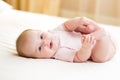 Happy baby girl lying on white sheet and holding her legs Royalty Free Stock Photo