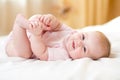 Happy baby girl lying on white sheet and holding her legs Royalty Free Stock Photo