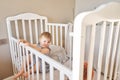 Happy baby girl one and half standing in the crib. Smiling 18 months child playing in sunny bedroom. Baby cot in Royalty Free Stock Photo