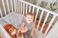 Happy baby girl one and half standing in the crib. Smiling 18 months child playing with toy monkey in sunny bedroom Royalty Free Stock Photo