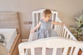 Happy baby girl one and half standing in the crib. Smiling 18 months child playing in sunny bedroom. Baby cot in Royalty Free Stock Photo