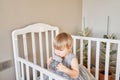 Happy baby girl drink water. Smiling 18 months child playing in sunny bedroom. Baby cot in the parent& x27;s bedroom Royalty Free Stock Photo