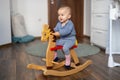 Happy baby girl playing on wooden rocking horse. Childhood, game at home concept