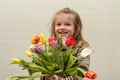 Happy baby girl rejoices and smiles with a bouquet of multi-colored tulips in hands Royalty Free Stock Photo