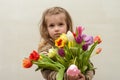 Happy baby girl rejoices and smiles with a bouquet of multi-colored tulips in hands Royalty Free Stock Photo