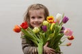 Happy baby girl rejoices and smiles with a bouquet of multi-colored tulips in hands Royalty Free Stock Photo