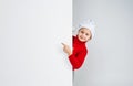 A happy baby girl in a Santa Claus hat looks out from behind an empty board isolated on a white background. layout Royalty Free Stock Photo