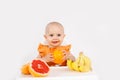 Happy baby girl sitting in high chair eating oranges in a white kitchen. Healthy nutrition for kids. Bio fruits as first solid Royalty Free Stock Photo