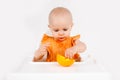 Happy baby girl sitting in high chair eating oranges in a white kitchen. Healthy nutrition for kids. Bio fruits as first solid Royalty Free Stock Photo