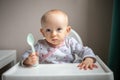 Happy baby girl with spoon sitting in highchair at home Royalty Free Stock Photo