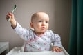 Happy baby girl with spoon sitting in highchair at home Royalty Free Stock Photo