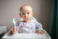 Happy baby girl with spoon sitting in highchair at home Royalty Free Stock Photo