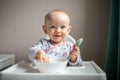 Happy baby girl with spoon sitting in highchair at home Royalty Free Stock Photo