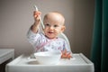 Happy baby girl with spoon sitting in highchair at home Royalty Free Stock Photo