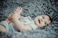 Happy baby holding her leg and lying on gray soft sheet Royalty Free Stock Photo