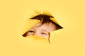 Happy baby in a hole on a paper yellow background. Torn child's head s Royalty Free Stock Photo