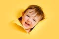 Happy baby in a hole on a paper yellow background. Torn child\'s head s Royalty Free Stock Photo