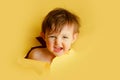 Happy baby in a hole on a paper yellow background. Torn child\'s head s Royalty Free Stock Photo