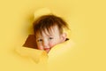 Happy baby in a hole on a paper yellow background. Torn child's head s Royalty Free Stock Photo