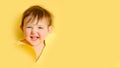 Happy baby in a hole on a paper yellow background. Torn child\'s head s Royalty Free Stock Photo