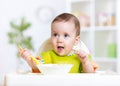 Happy baby kid eating food itself with spoon