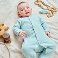 Happy baby lies on a blanket in mint color clothes with wooden toys. Smiling child in turquoise pajamas, top view