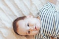 Happy baby lying on white sheet and holding her legs. Playful baby lying down in bed Royalty Free Stock Photo