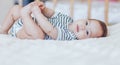 Happy baby lying on white sheet and holding her legs. Playful baby lying down in bed Royalty Free Stock Photo