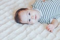 Happy baby lying on white sheet and holding her legs. Playful baby lying down in bed Royalty Free Stock Photo