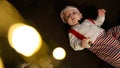 A happy baby in a red Santa Claus hat is lying on the floor, smiling happily and laughing on a dark background Royalty Free Stock Photo