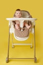 Happy baby sits on a high chair for feeding children, studio yellow background. Smiling child boy at the age of six months eating Royalty Free Stock Photo