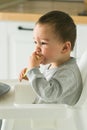 Happy baby sitting in high chair eating fruit in kitchen. Healthy nutrition for kids. Bio carrot as first solid food for Royalty Free Stock Photo