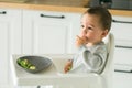 Happy baby sitting in high chair eating fruit in kitchen. Healthy nutrition for kids. Bio carrot as first solid food for Royalty Free Stock Photo