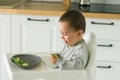 Happy baby sitting in high chair eating fruit in kitchen. Healthy nutrition for kids. Bio carrot as first solid food for Royalty Free Stock Photo