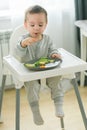 Happy baby sitting in high chair eating fruit in kitchen. Healthy nutrition for kids. Bio carrot as first solid food for Royalty Free Stock Photo