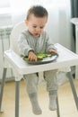 Happy baby sitting in high chair eating fruit in kitchen. Healthy nutrition for kids. Bio carrot as first solid food for Royalty Free Stock Photo