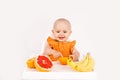 Happy baby sitting in high chair eating fruits in a white kitchen. Healthy nutrition for kids. Children eat oranges and Royalty Free Stock Photo