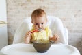 Happy baby sitting in highchair and eating greek yogurt Royalty Free Stock Photo