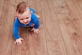 Happy baby toddler crawls on a wooden laminate. Funny child on the parquet in the home living room, aged 6-11 months Royalty Free Stock Photo