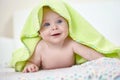 Happy baby under a green towel after bathing
