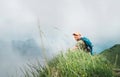 Happy backpacker man has a rest break enjoying cloudy valley bottom walking by the foggy cloudy weather mountain range . Active Royalty Free Stock Photo