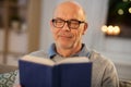 Happy bald senior man on sofa reading book at home Royalty Free Stock Photo