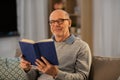 Happy bald senior man on sofa reading book at home Royalty Free Stock Photo