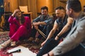 Happy band members sit on colourful carpet and write music and lyrics to their next song. Interior of recording studio.