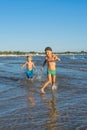 Happy barefoot family having fun Ã¢â¬â two brothers together run with splashes by water pool along surf of sunset sea beach. Active Royalty Free Stock Photo