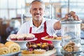 Happy barista smiling at camera behind plates of cakes