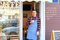 Happy barista standing at cafe entrance, portrait of mature business man attend new customers in his coffe shop