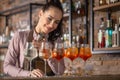 Happy bartender makes aperol spritz cocktail on a bar into five glasses