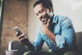 Happy bearded African businessman using phone while sitting on sofa at his modern home. Concept of young people working Royalty Free Stock Photo