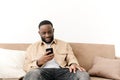 Happy bearded afro american freelancer working using phone while sitting on sofa at his home. Concept of young people Royalty Free Stock Photo